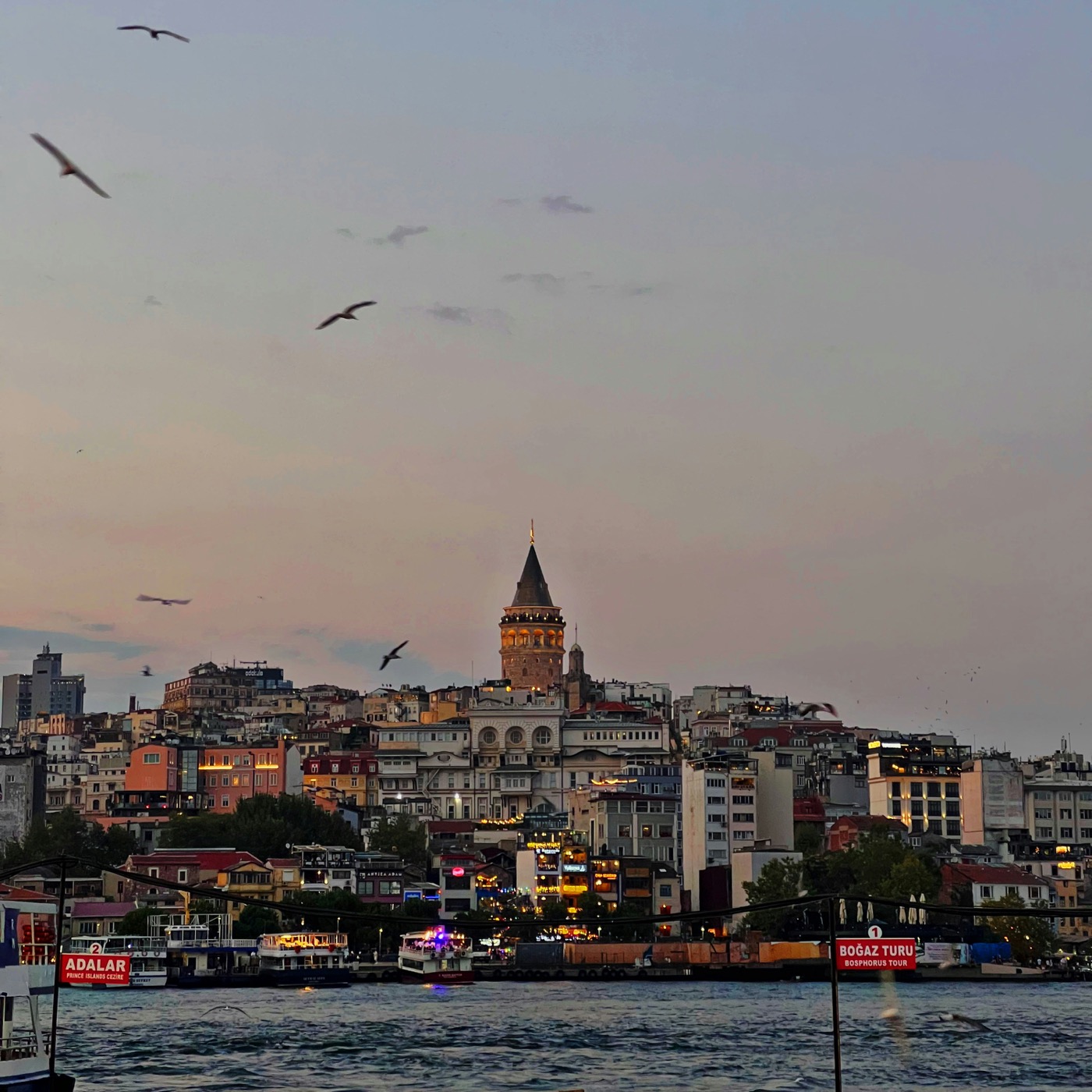 Galata Tower rising above Beyoglu rooftops in warm golden-hour light before sunset.